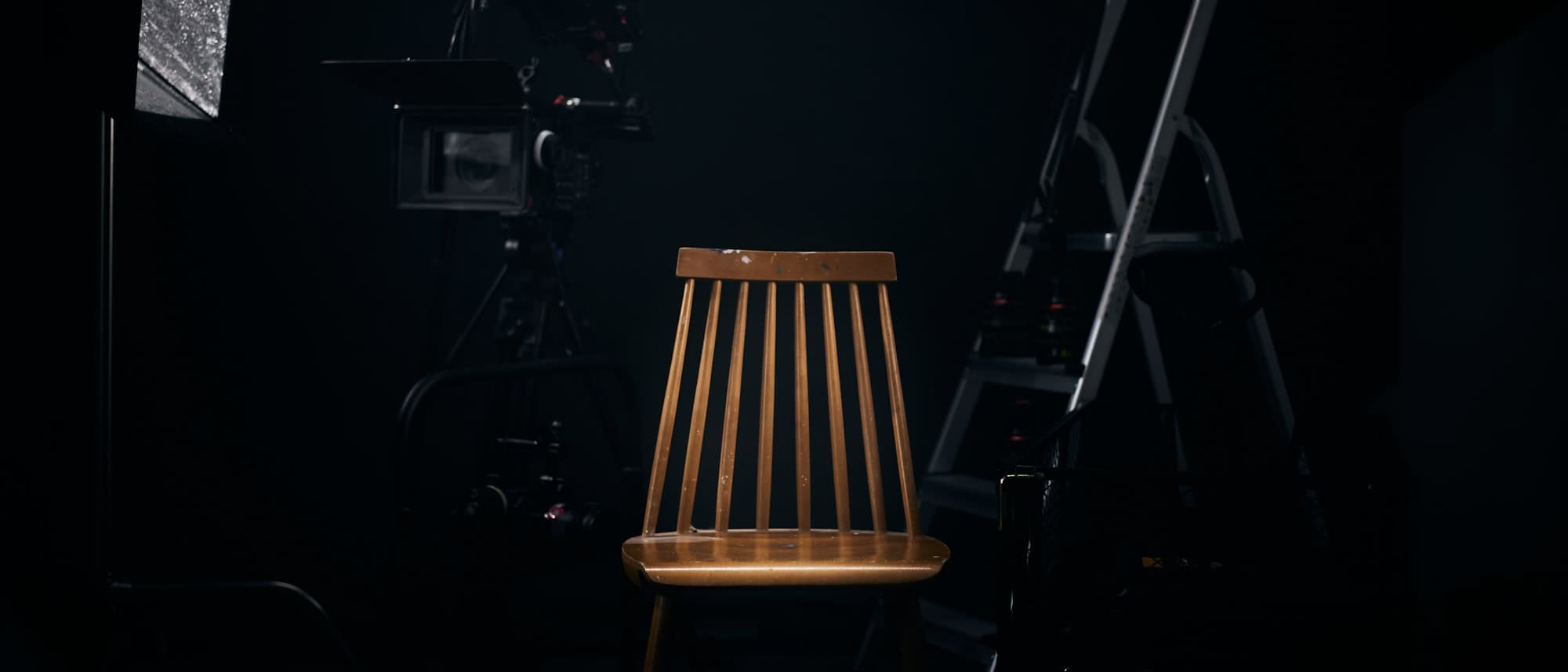 An empty wooden chair lit by a single light on a dark film set